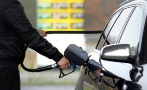Muž v černé bundě čerpá naftu do nádrže osobního vozu